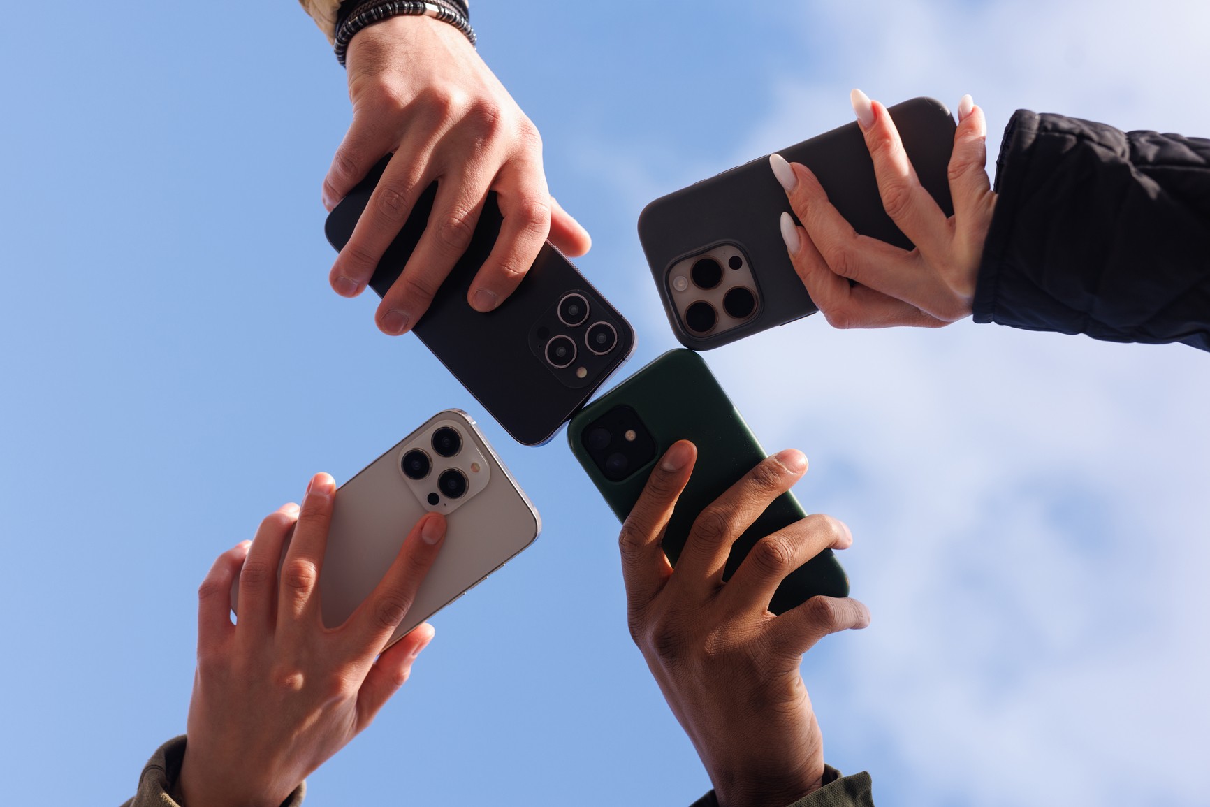 Four hands holding phones up against the sky