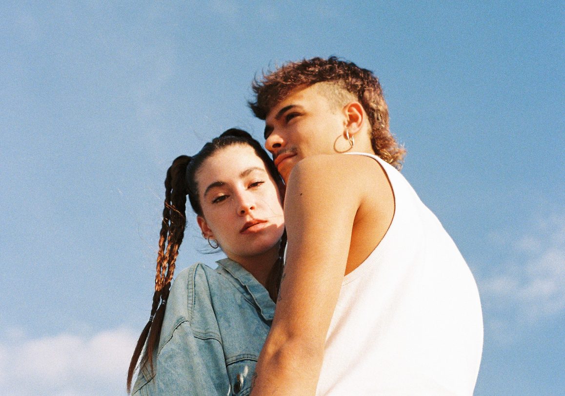 Two people standing close together against a blue sky