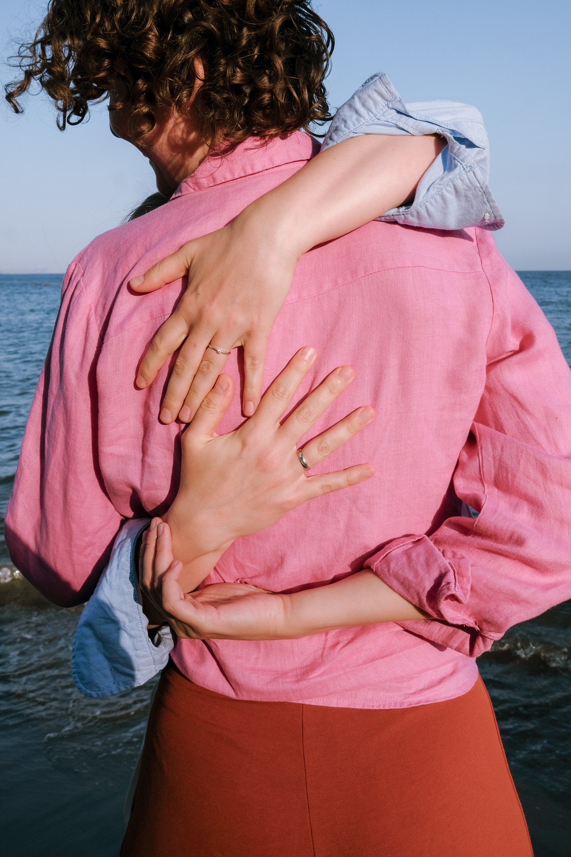 A hug by the sea, with hands resting on a pink shirt