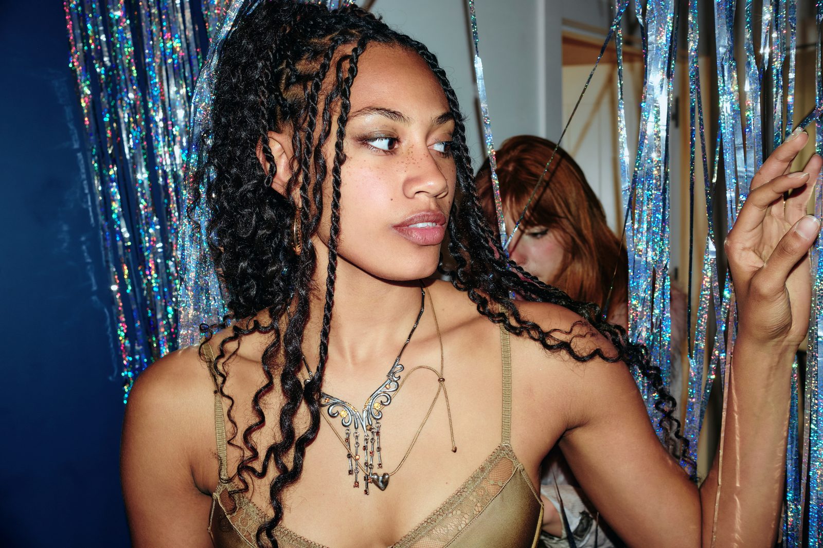 A person with braids standing beside a silver tinsel curtain